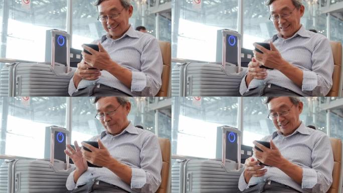 亚洲高级男子看着手机屏幕微笑。他坐在机场。旅行，人，旅程，全球，生活方式，假期，技术概念。在机场