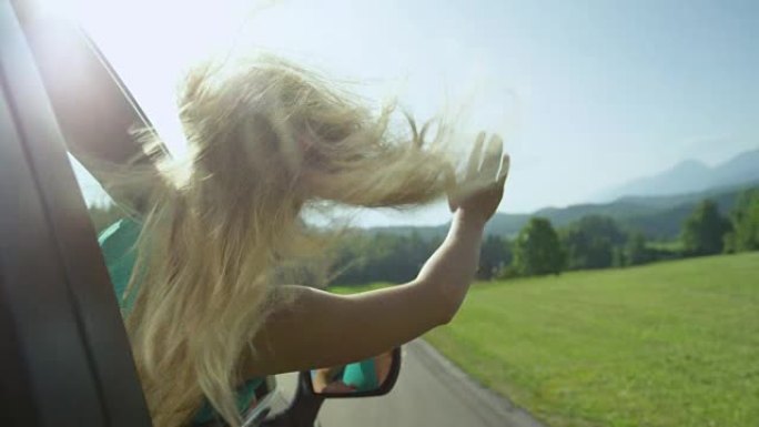 慢动作: 年轻的金发女子在开车时在空中挥舞手臂。