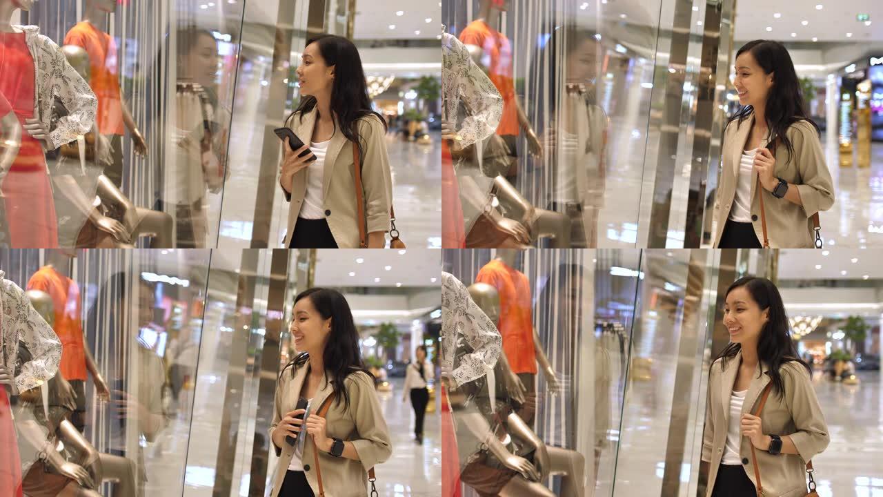 年轻的亚洲购物女人停下来看着商店的橱窗