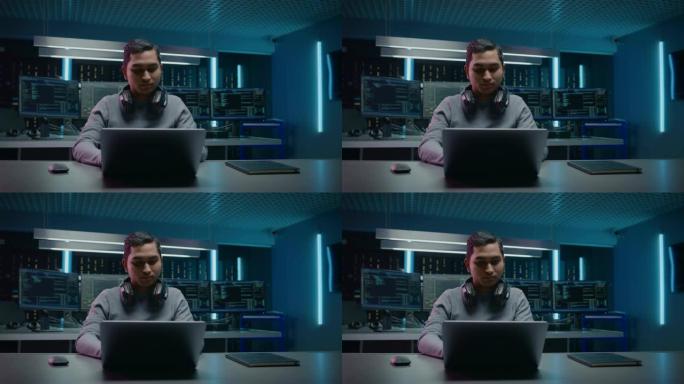 英俊的印度软件开发人员/黑客/游戏玩家坐在办公桌前，在笔记本电脑上工作/玩耍的肖像。在背景中，具有多