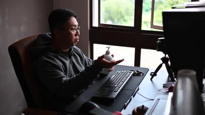 一位亚洲华人男性在他家里的自习室里写博客，教授如何正确使用洗手液，并向他的网络客户销售产品