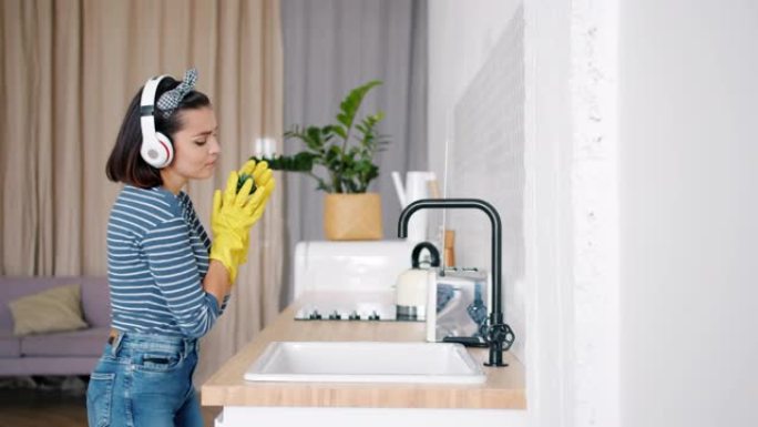 快乐的女孩戴着耳机在厨房打扫时在室内植物里唱歌
