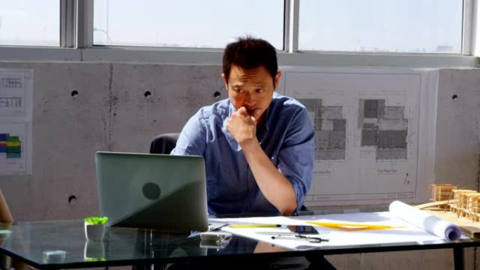 亚洲男性建筑师在现代办公室4k桌上使用笔记本电脑的前视图