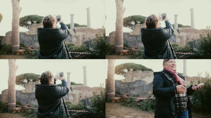 兴奋快乐的微笑欧洲高级妇女在度假旅行中拍摄意大利奥斯蒂亚古柱遗址的电话照片。