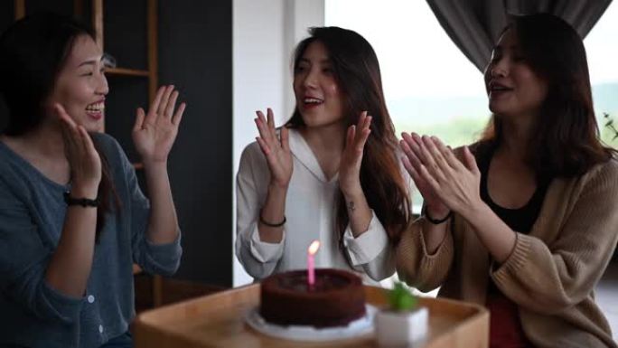 一位亚洲华裔年轻美女在她的公寓里和朋友一起庆祝生日蛋糕