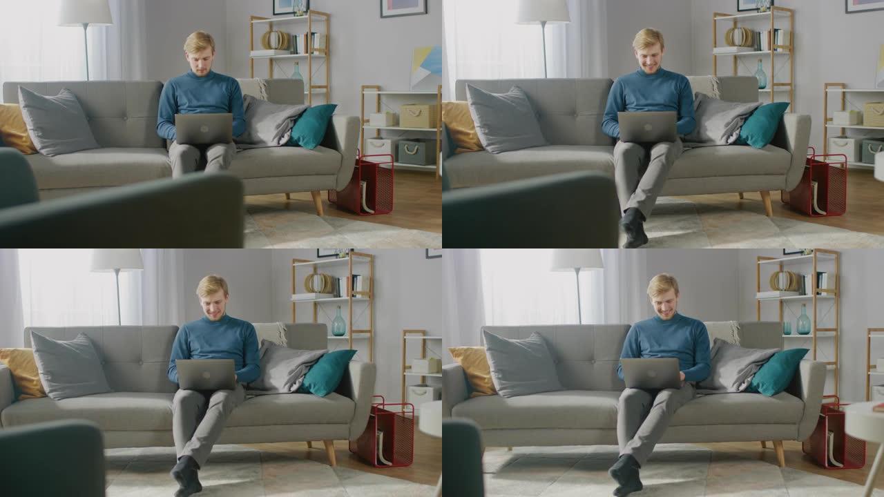 英俊的金发小伙子在笔记本电脑上工作的肖像，而坐在他舒适的客厅的沙发上。创意自由职业者在家放松，浏览互