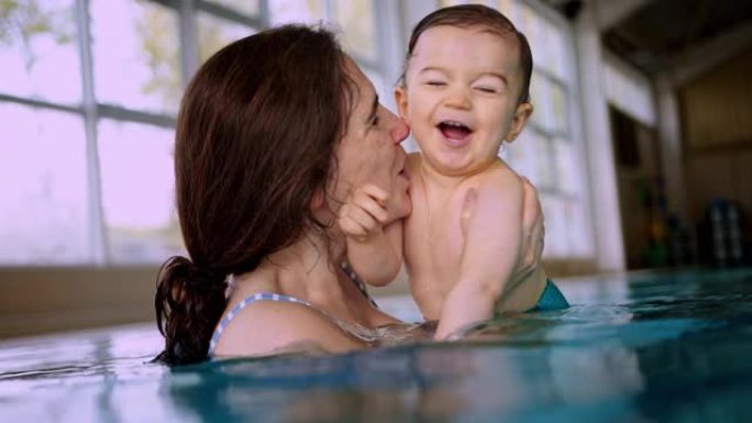 母亲吹吻婴儿在室内游泳池游泳