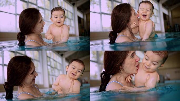 母亲吹吻婴儿在室内游泳池游泳