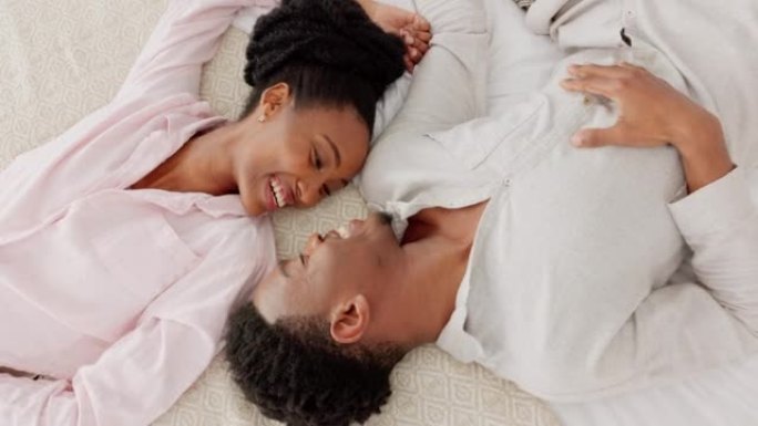 幸福的黑人夫妇在床上结伴，在卧室里交谈，放松和欢笑。在年轻的男人和女人之上，分享一个充满爱，浪漫的时