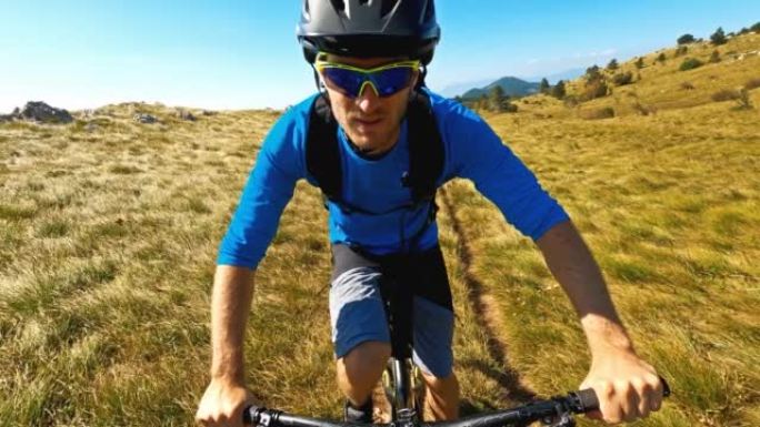 男子在山高绿草的岩石自行车道上骑自行车的肖像