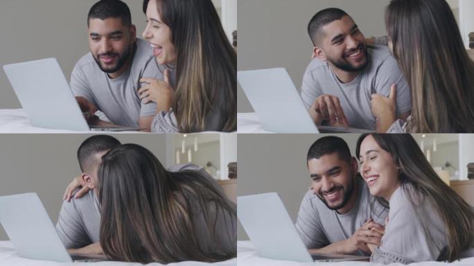 一对年轻的幸福夫妇在一起躺在床上时使用笔记本电脑并选择了新家。兴奋的情侣在网上购物，网上预订。千禧一