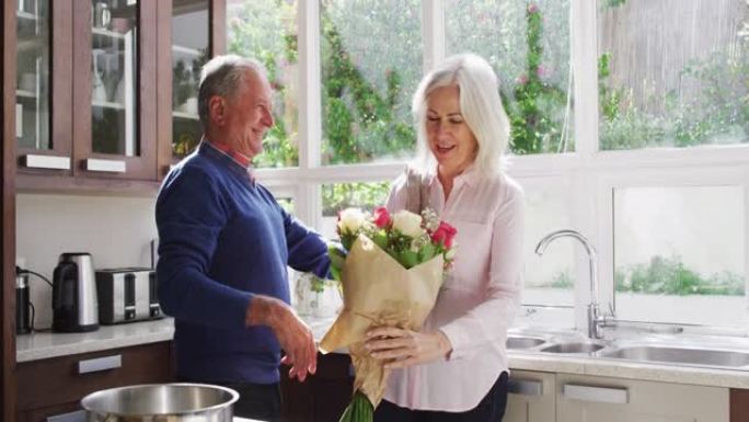 高级男子给妻子一束鲜花，并在家里的厨房里拥抱她