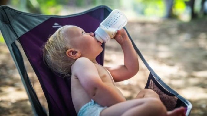 蹒跚学步的孩子在野营椅上喝奶瓶中的牛奶