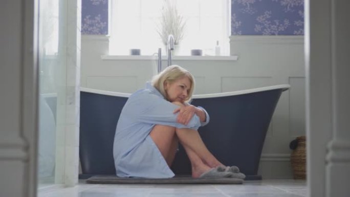 患有失禁的更年期成熟女性坐在家里浴室的地板上-慢动作拍摄