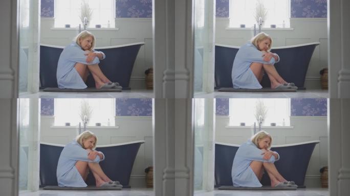 患有失禁的更年期成熟女性坐在家里浴室的地板上-慢动作拍摄