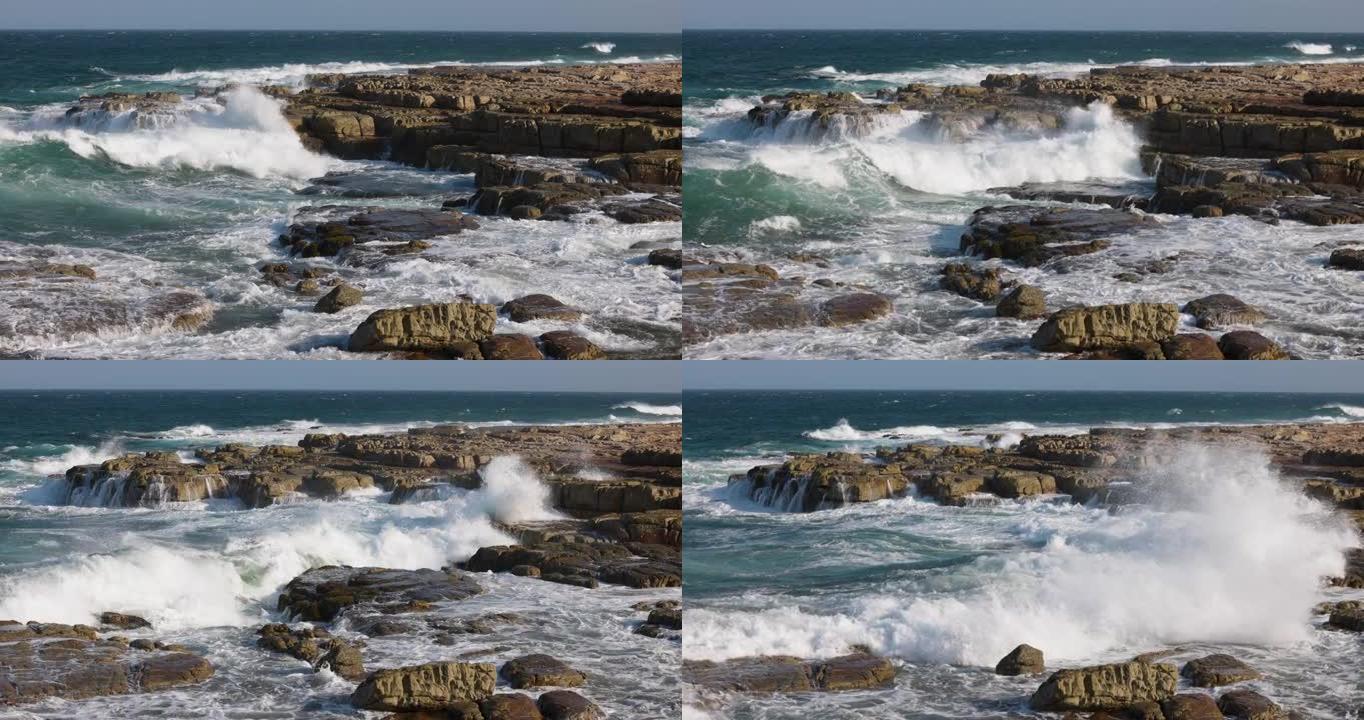 在岩石海岸线上冲破岩石的波浪的空中慢动作视图