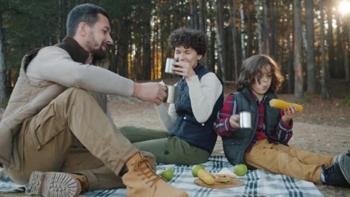 父母和儿子在森林紧贴杯中享受野餐，烘烤健康食品