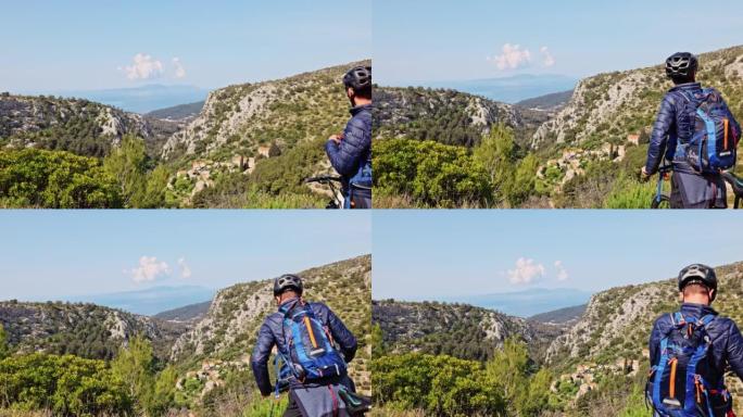 戴着头盔的男子骑自行车休息一下，站在山顶上喝酒，看着赫瓦尔岛的景色