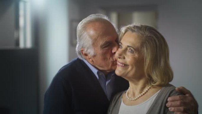 可爱的幸福成熟夫妇的电影镜头正在享受拥抱和亲吻的时光，这是家里客厅里永恒爱情的标志。概念: 爱情，家