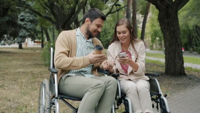 在公园里坐在轮椅上说话和使用智能手机的残疾年轻人的慢动作