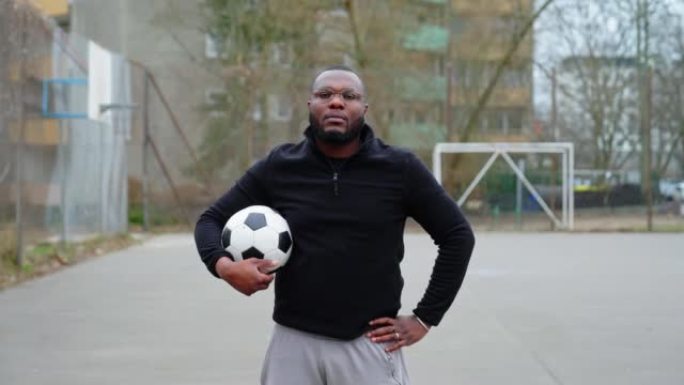 自信的非洲男子站在运动场上拿着足球的肖像