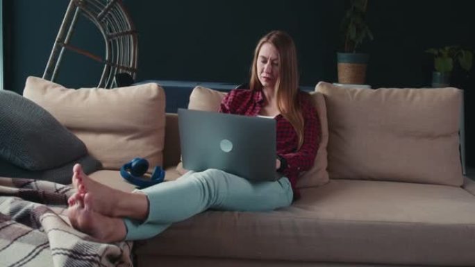 在家工作。美丽严肃紧张的年轻自由职业者女商人在家里舒适的沙发上使用笔记本电脑。