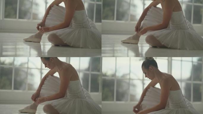 优雅的芭蕾舞女演员系芭蕾舞鞋，训练前坐在地板上思考。年轻的专业女舞者准备她的脚鞋在工作室里表演。