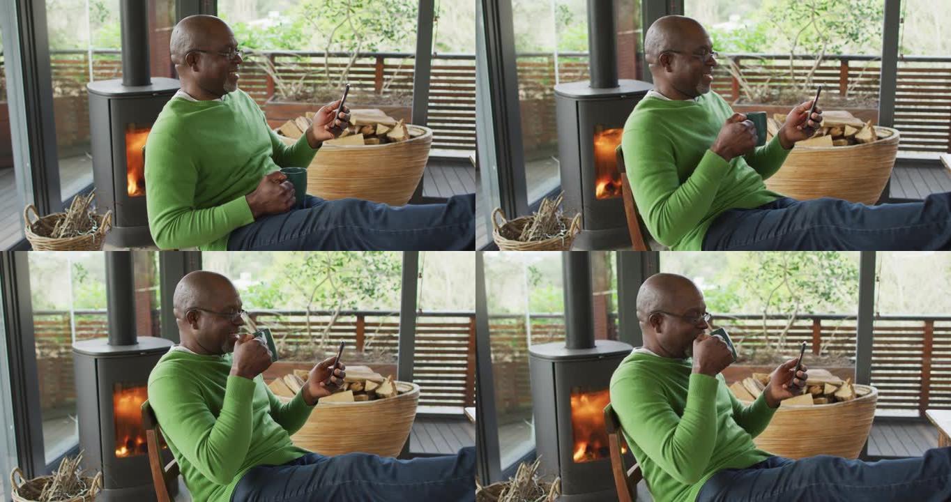 微笑的非洲裔美国高级男子双脚放松，使用智能手机和喝咖啡
