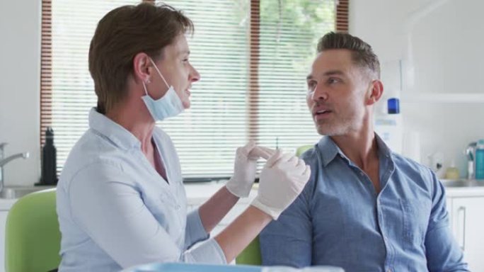 在现代牙科诊所，戴着口罩的高加索女牙科护士与男性患者交谈