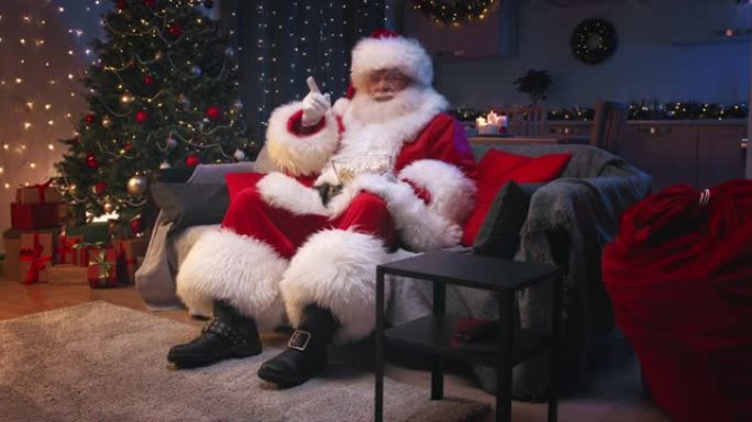 圣诞老人坐在装饰精美的客厅里过圣诞节，坐在灰色的沙发上看电视，吃着爆米花。圣诞老人对电影的情节做出了