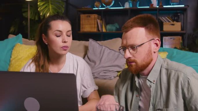 年轻积极的白人男女一起合作交谈，看着现代灯光之家的笔记本电脑屏幕