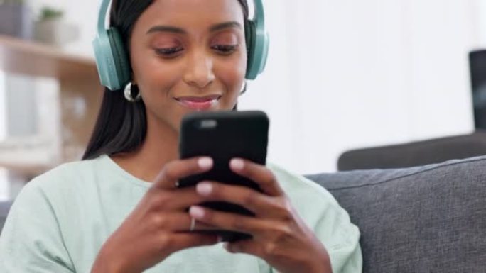女孩，带有耳机和音乐的电话和社交媒体，使用智能手机在互联网上阅读通知，并在家里的沙发上微笑。在移动应