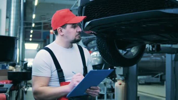 汽车修理工检查汽车的底面并做笔记。汽车维修公司的汽车修理工。