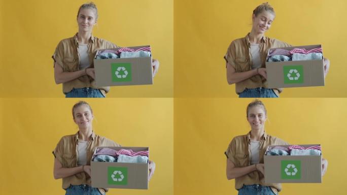 黄色背景下年轻女子拿着纸板箱和旧衣服回收的慢动作