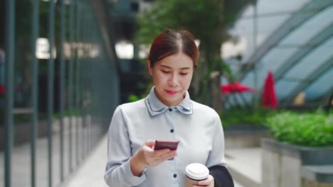 年轻的女商人在城市散步时使用手机和喝咖啡