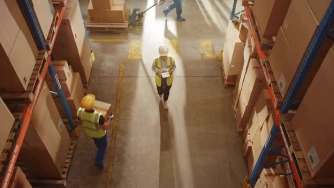 自上而下的提升视图: 戴着安全帽的工人在装满货物的货架的零售仓库中使用数字平板电脑检查库存和库存。从