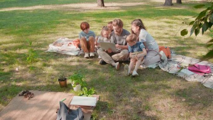 小学生在公园里用笔记本电脑聚集在老师周围