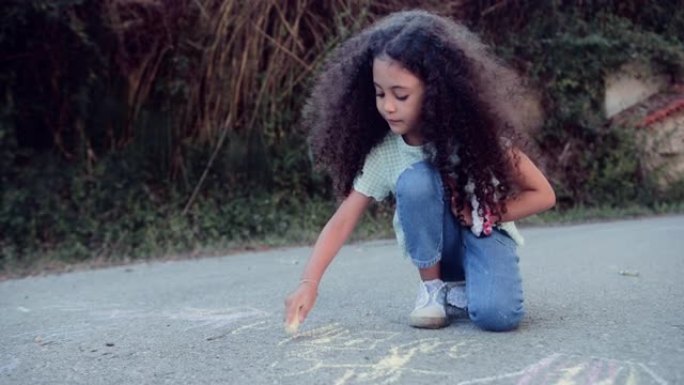 可爱的小女孩用粉笔在柏油路上画画