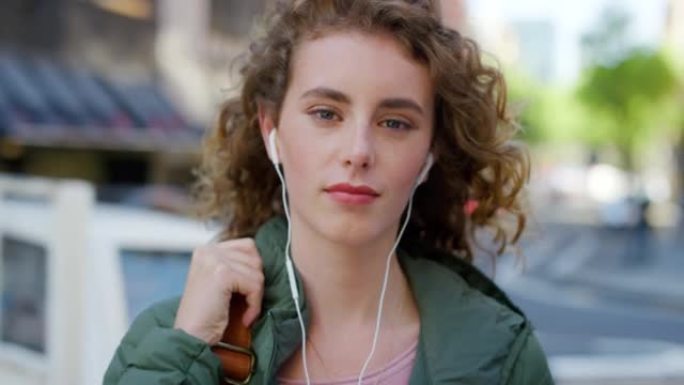 一个年轻自信的女学生早上在外面用耳塞听音乐。一个美丽而前卫的女人的肖像，卷发，在城市里享受着带耳机的