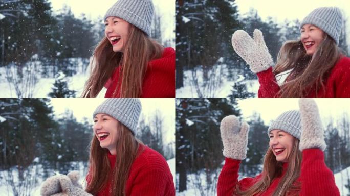 享受冬天。穿着红色毛衣的美丽年轻快乐快乐兴奋的女人在森林慢动作的连指手套上吹雪。