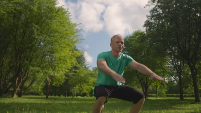 穿着绿松石t恤的中年斯堪的纳维亚运动员在早晨的阳光下蹲在公园里