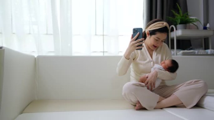 美丽的妈妈抱着可爱的小新生儿在手机上做视频通话。技术