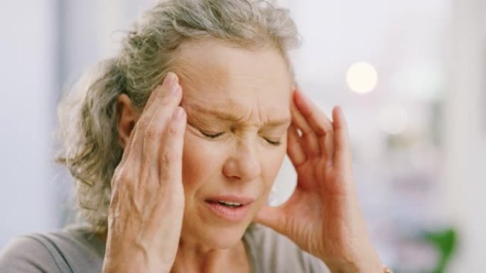 头痛的高级妇女在痛苦中摩擦额头。面对一位压力大，疲倦和焦虑的女士，由于慢性偏头痛而感到不适，无法集中