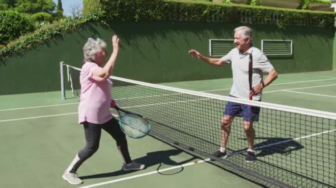 快乐的高加索高级夫妇在打了一场比赛后在室外网球场击掌
