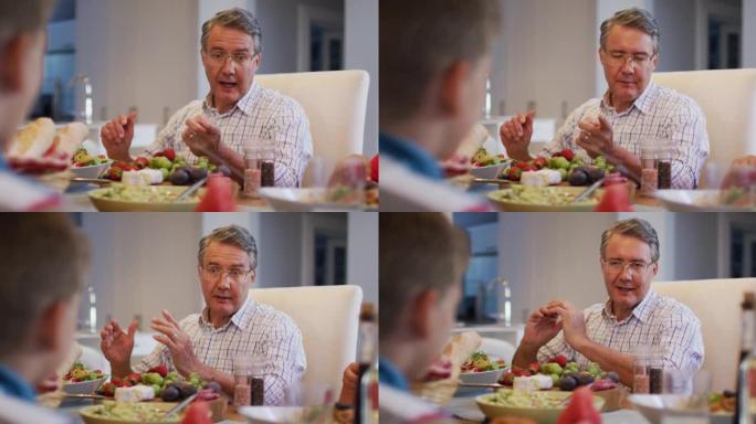 微笑的高加索祖父在家庭用餐时在餐桌上与孙子交谈