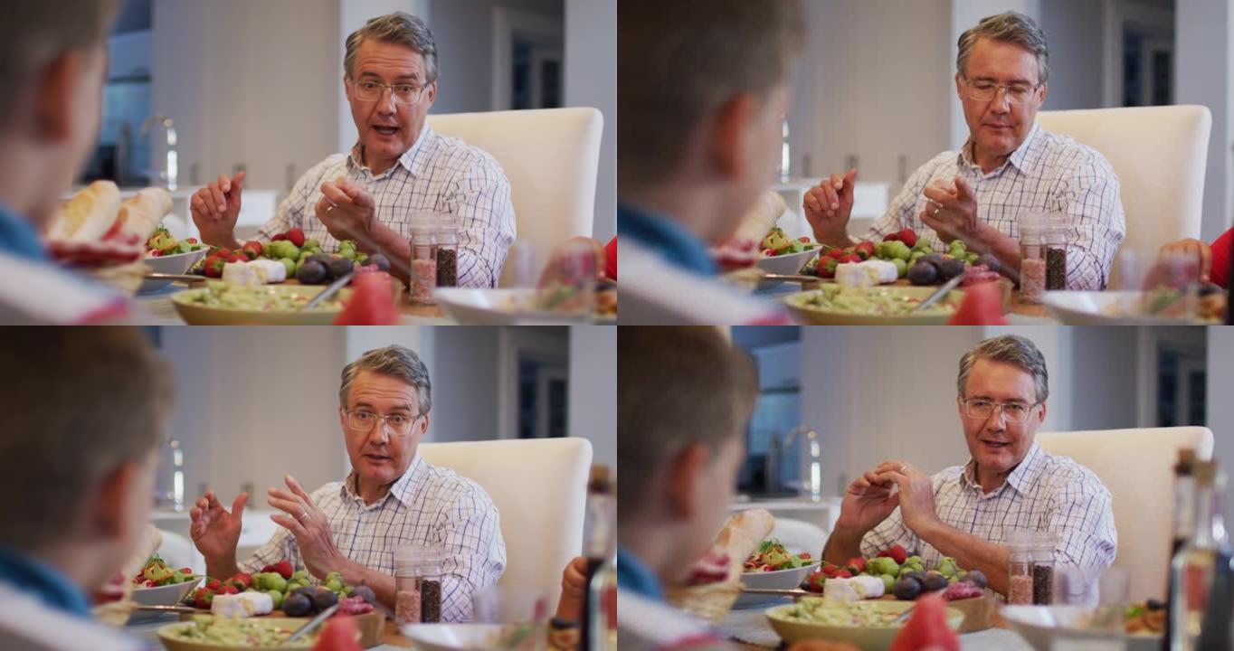 微笑的高加索祖父在家庭用餐时在餐桌上与孙子交谈