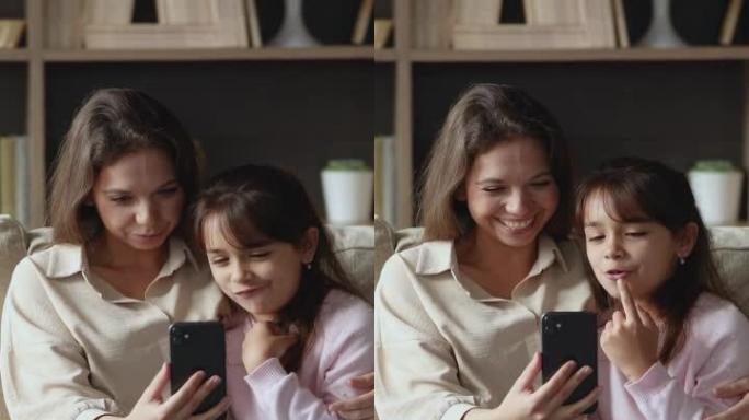 妈妈和女儿用智能手机坐在家里的沙发上