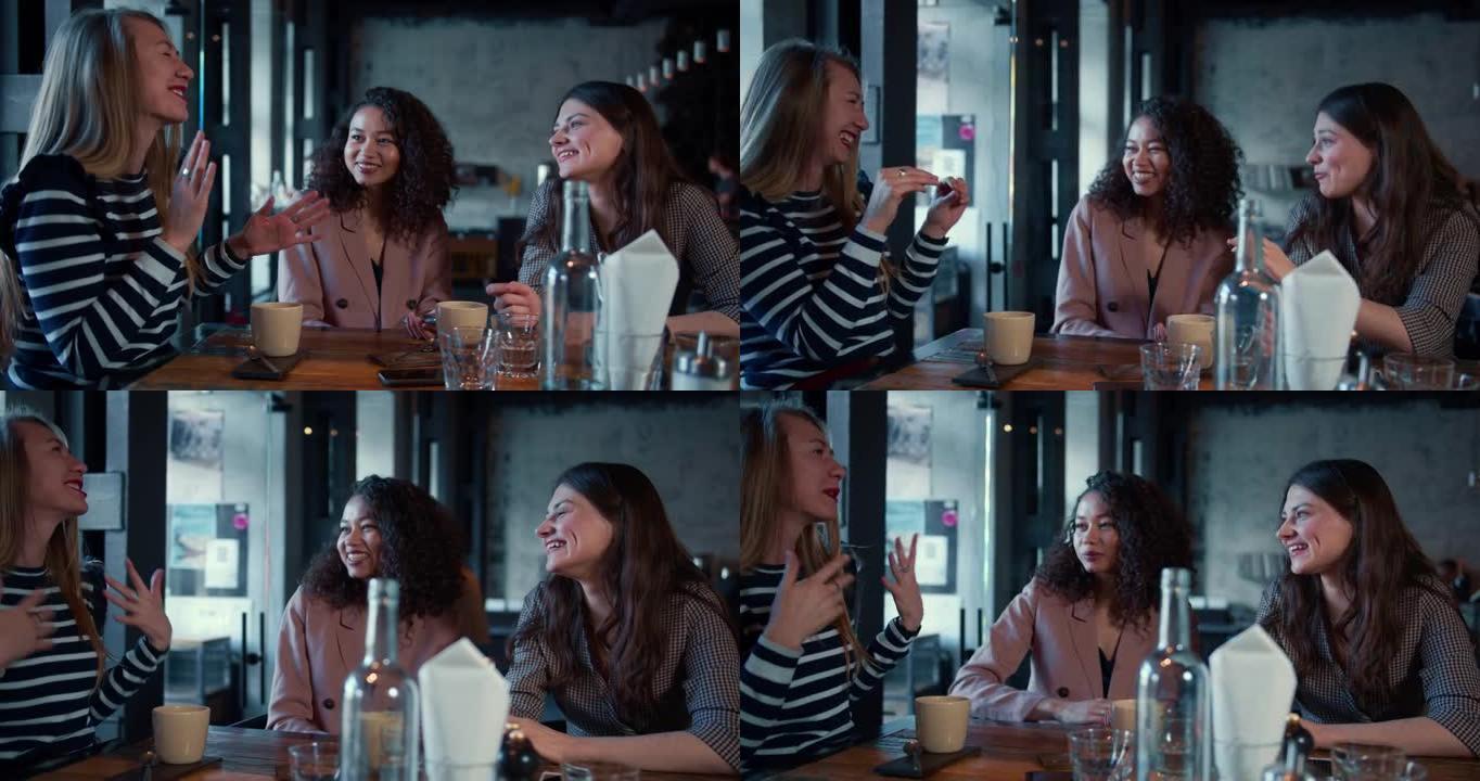 电影拍摄的三个美丽的年轻快乐的多民族女性朋友微笑着，在时尚的咖啡桌旁随意交谈。