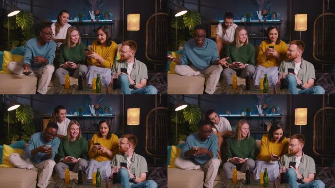 快乐的多民族年轻朋友一起坐在沙发上，使用智能手机在家里讨论有趣的互联网社交媒体。