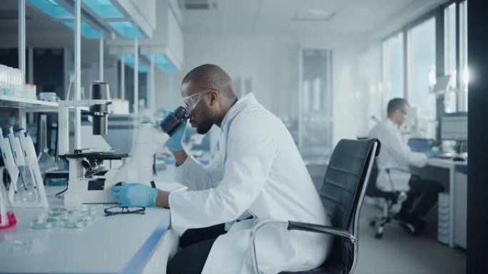 医学发展实验室: 黑人男性科学家在显微镜下观察，分析培养皿样本的肖像。在高级科学实验室从事研究的专业